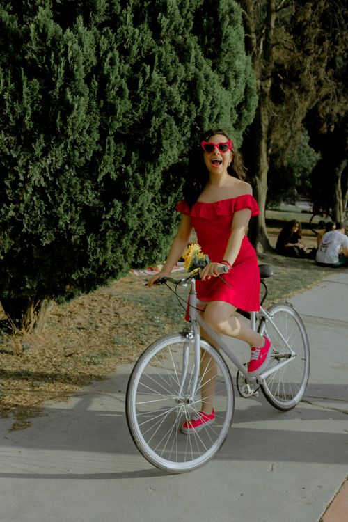 Free Smiling woman in red dress riding bicycle in sunny park. Stock Photo