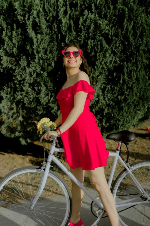 Free Smiling woman in a red dress riding a bicycle in a sunny park setting. Stock Photo