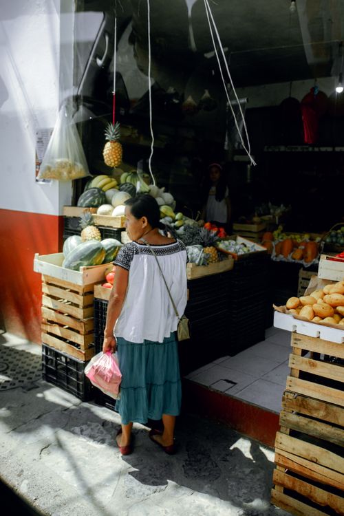 Free A woman in traditional attire shops for fresh fruits and vegetables at a local market stall. Stock Photo