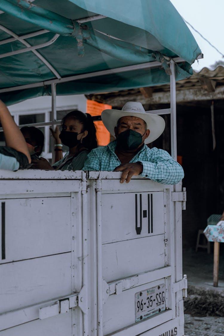 People In Face Masks Sitting On The Back Of A Truck 