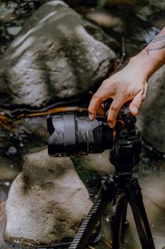 Close-up of a person's hand adjusting a camera on a tripod near rocks.