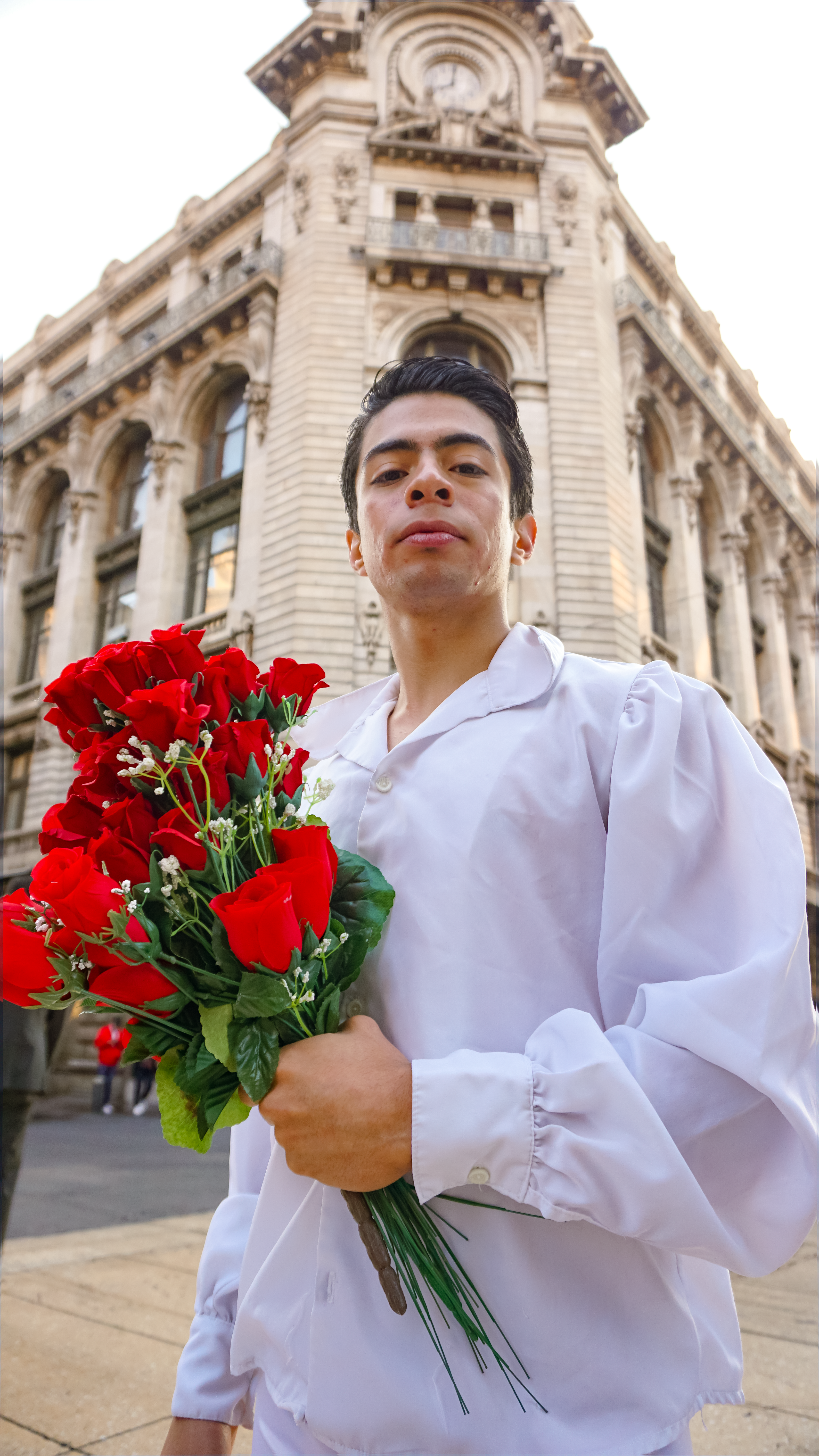 Portrait of a man in a white shirt holding red roses at a historic building in Mexico City.