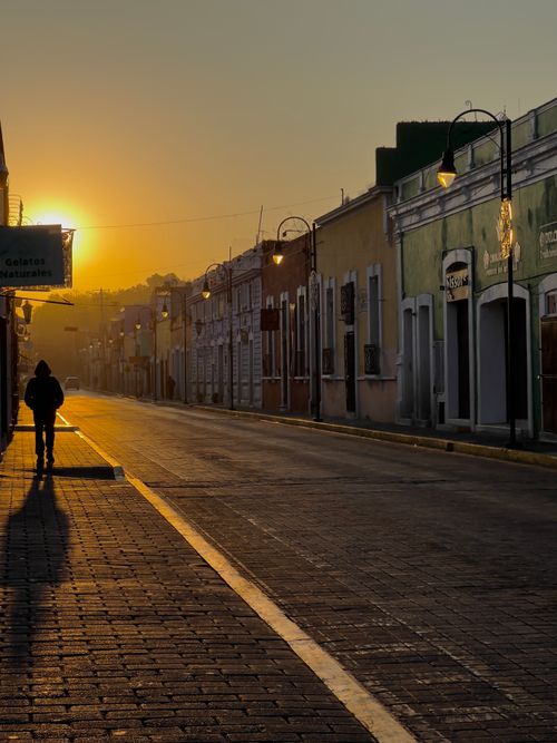 Free Silhouetted person walking down a Cholula street at sunrise. Vibrant colors on historic buildings. Stock Photo