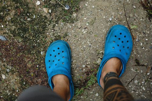 Free Close-up of tattooed feet wearing blue rubber clogs outdoors. Top-down view. Stock Photo