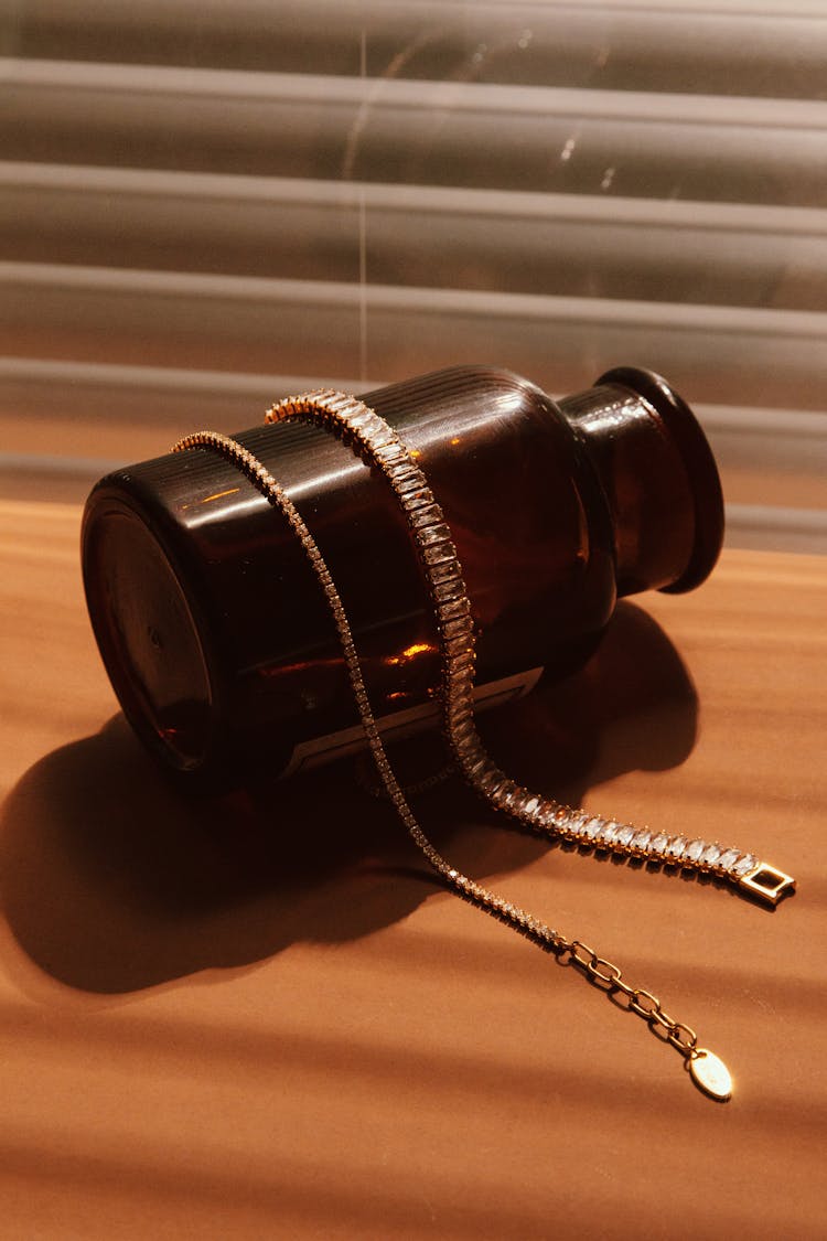 Gold Necklace And Bracelet On Top Of A Brown Bottle