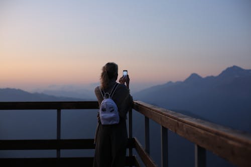 Woman in Brown Long Sleeve Shirt Taking a Picture of the Mountains