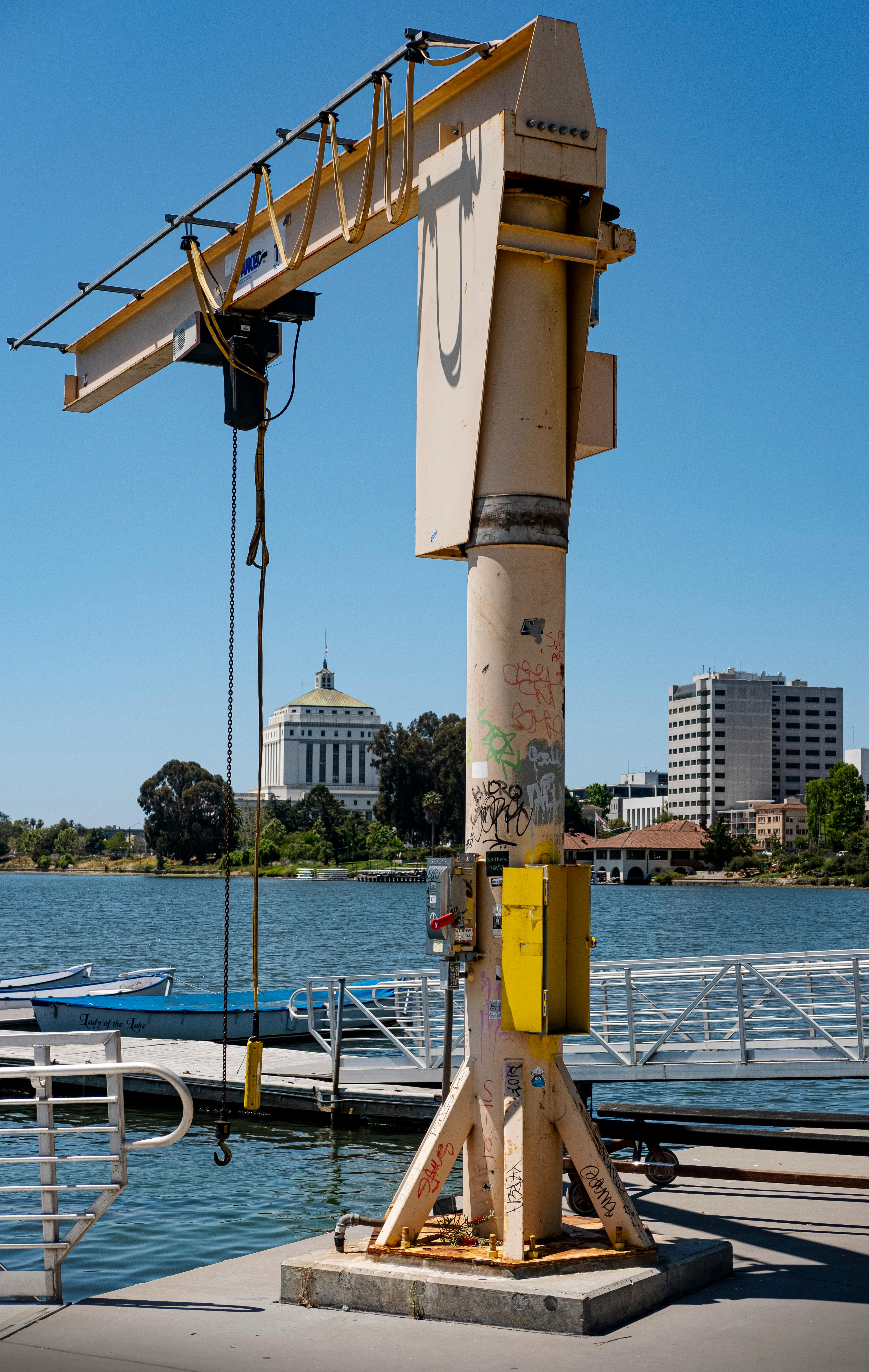 A dockside crane against a city backdrop with clear skies and calm water.
