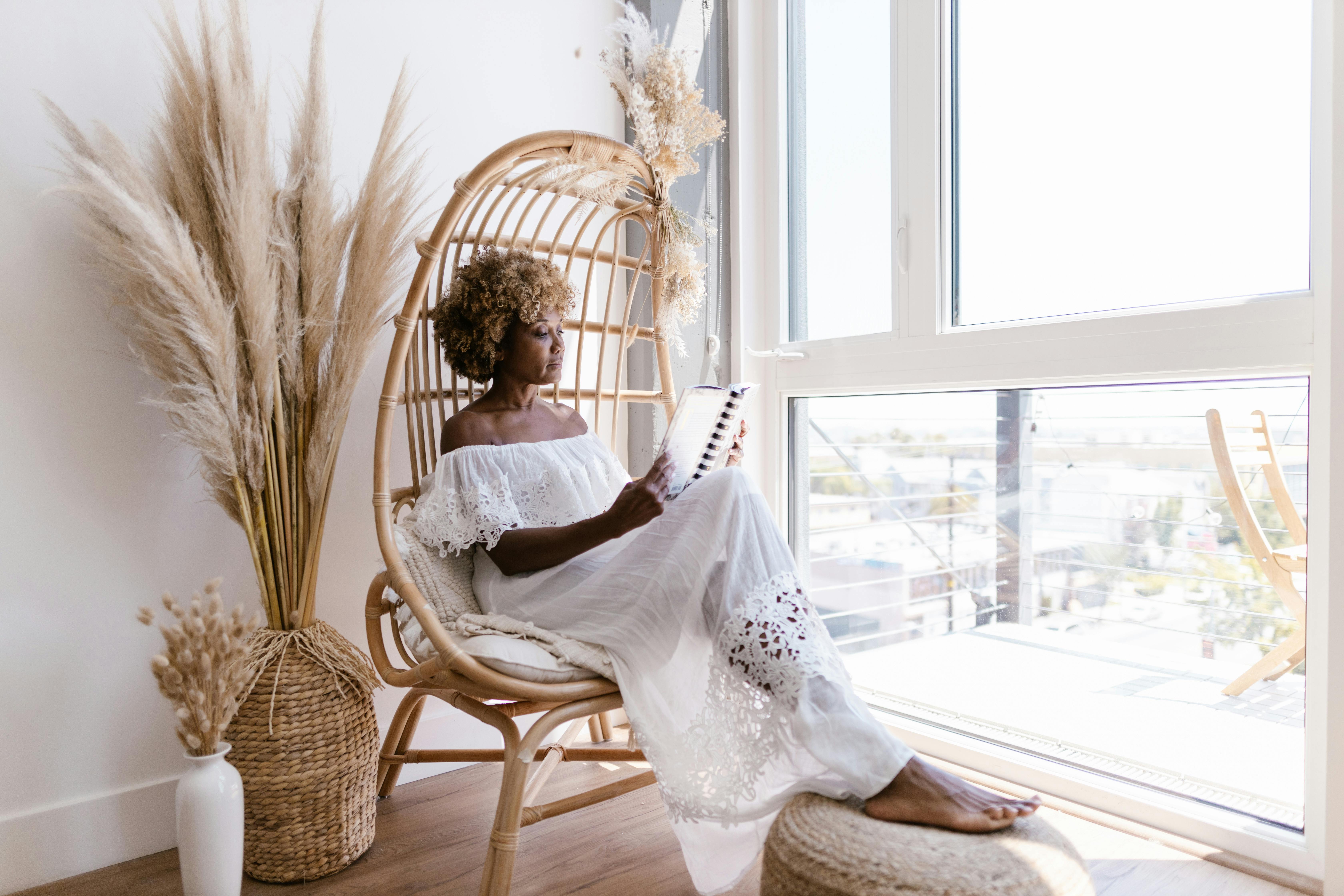 woman with afro and white dress reading on a basket chair