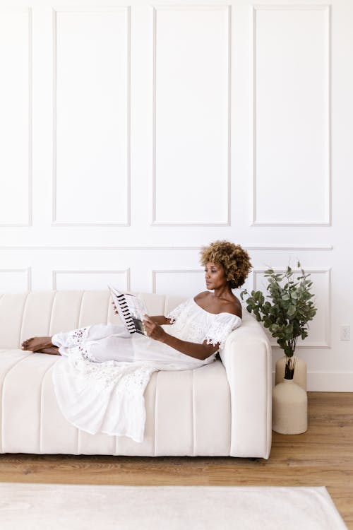 Woman in White Dress Lying Down on Sofa and Reading