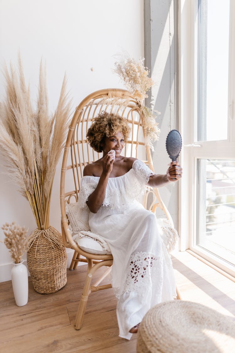 Woman With Afro Hairstyle Sitting On A Basket Chair And Looking At A Mirror