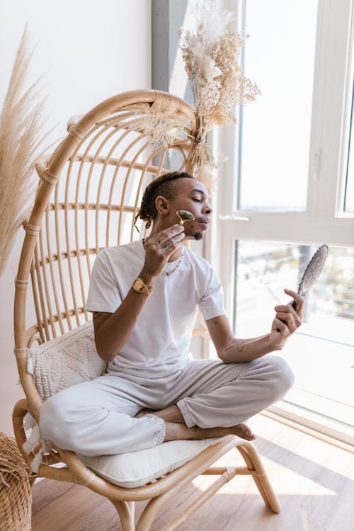 Man Sitting on a Basket Chair and Making Face Massage with a Face Roller
