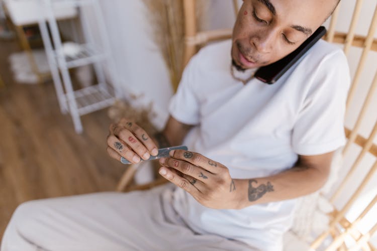 Man Talking Through A Phone While Filing His Nails 