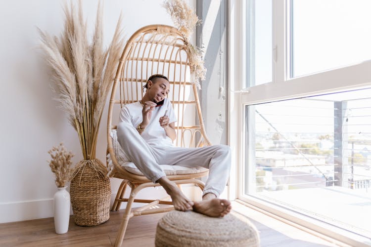 Man Talking On The Phone While Sitting Beside Window And Filing His Nails