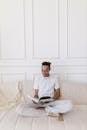 Man in White Polo Shirt Reading Book Sitting on White Couch