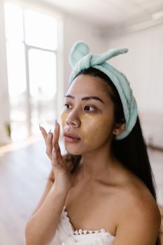 Woman with a headband applies skincare indoors, focusing on beauty and wellness.