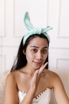 Young Asian woman applying face cream for skincare routine indoors.