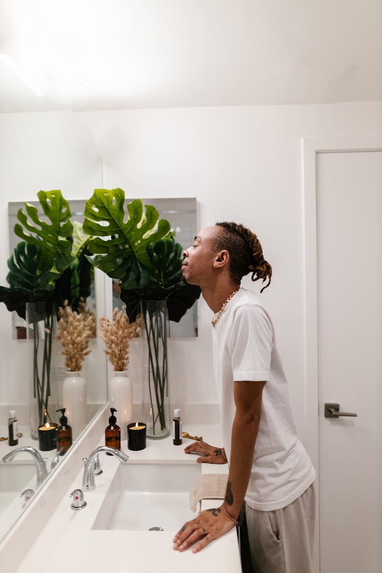 Man With Dreadlocks Looking At A Mirror In A White Bathroom