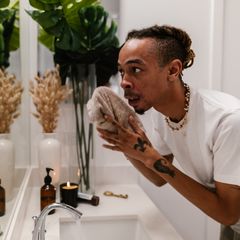 A man freshening up with a towel at a bright bathroom sink
