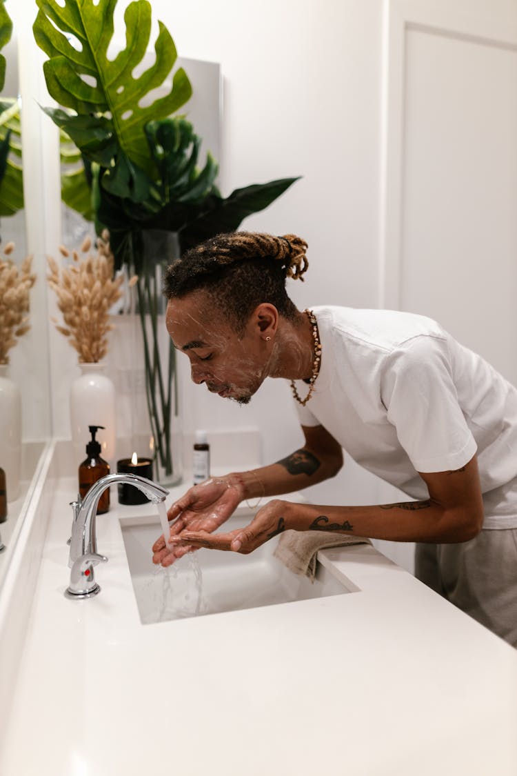 Man With Dreadlocks Washing His Face At Sink