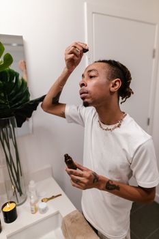 A man applies skincare serum using a dropper in a modern bathroom setting.