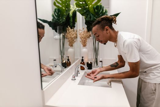 A man maintaining hygiene in a stylish bathroom with plants and candles.