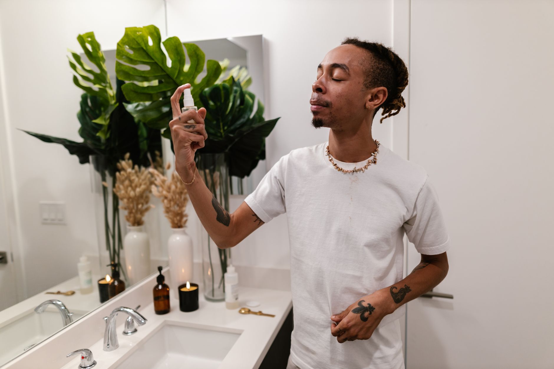 A man applying hydrating face mist in a modern bathroom setting for skincare routine.