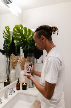 A man in a white shirt applies skincare in a modern bathroom setting.