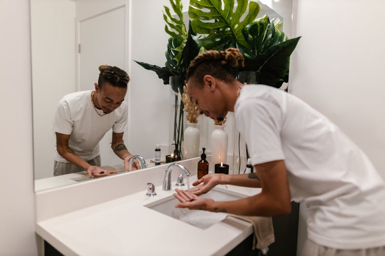 Young Man Washing Hands At Sink In Bathroom