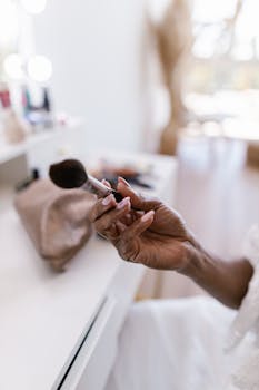 Close-up of a woman's hand holding a makeup brush in an airy and bright indoor setting.