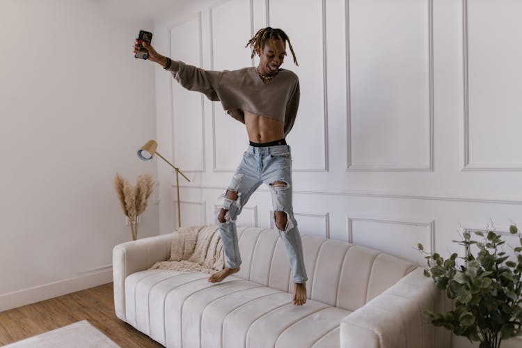 Happy Man With Cellphone Jumping On Sofa