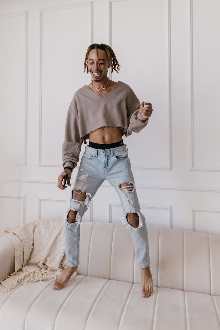 Man With Dreadlocks And Holes In Jeans Jumping On A Sofa