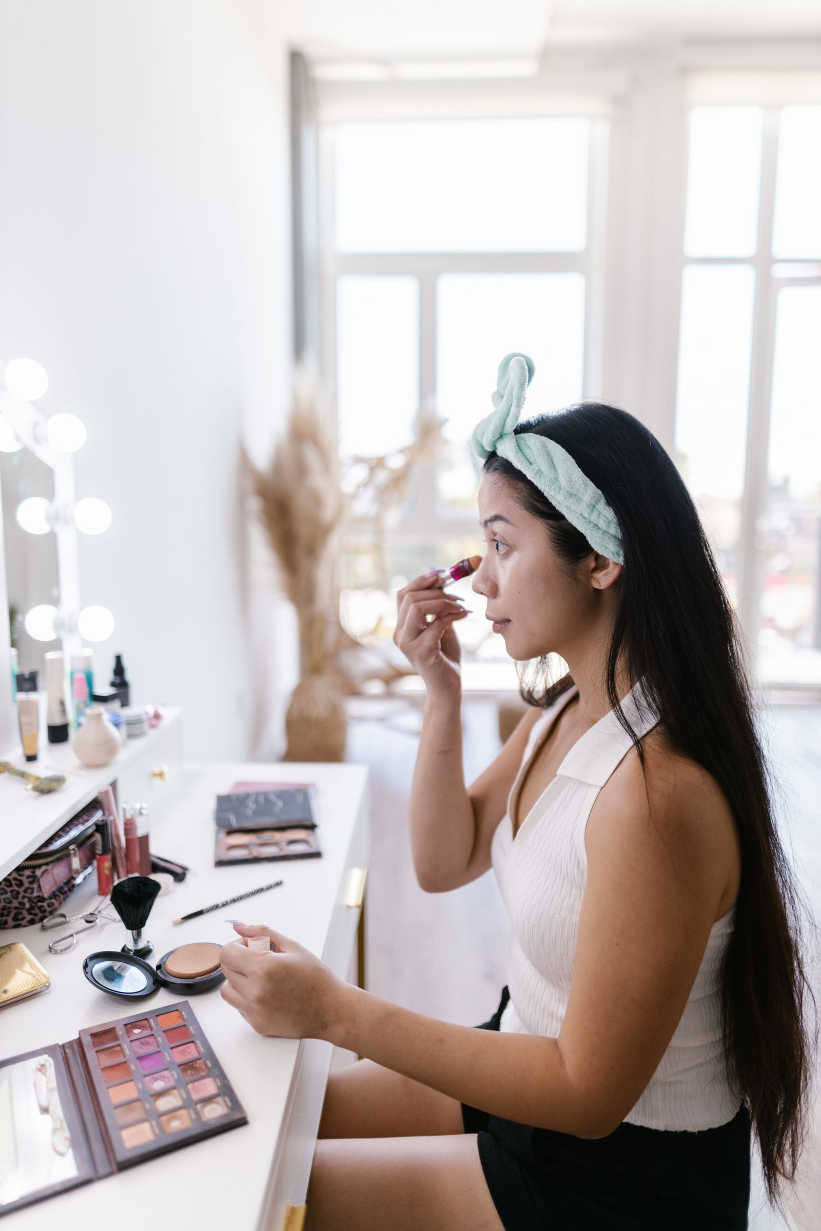 Woman applying makeup at a vanity with everyday beauty tools nearby