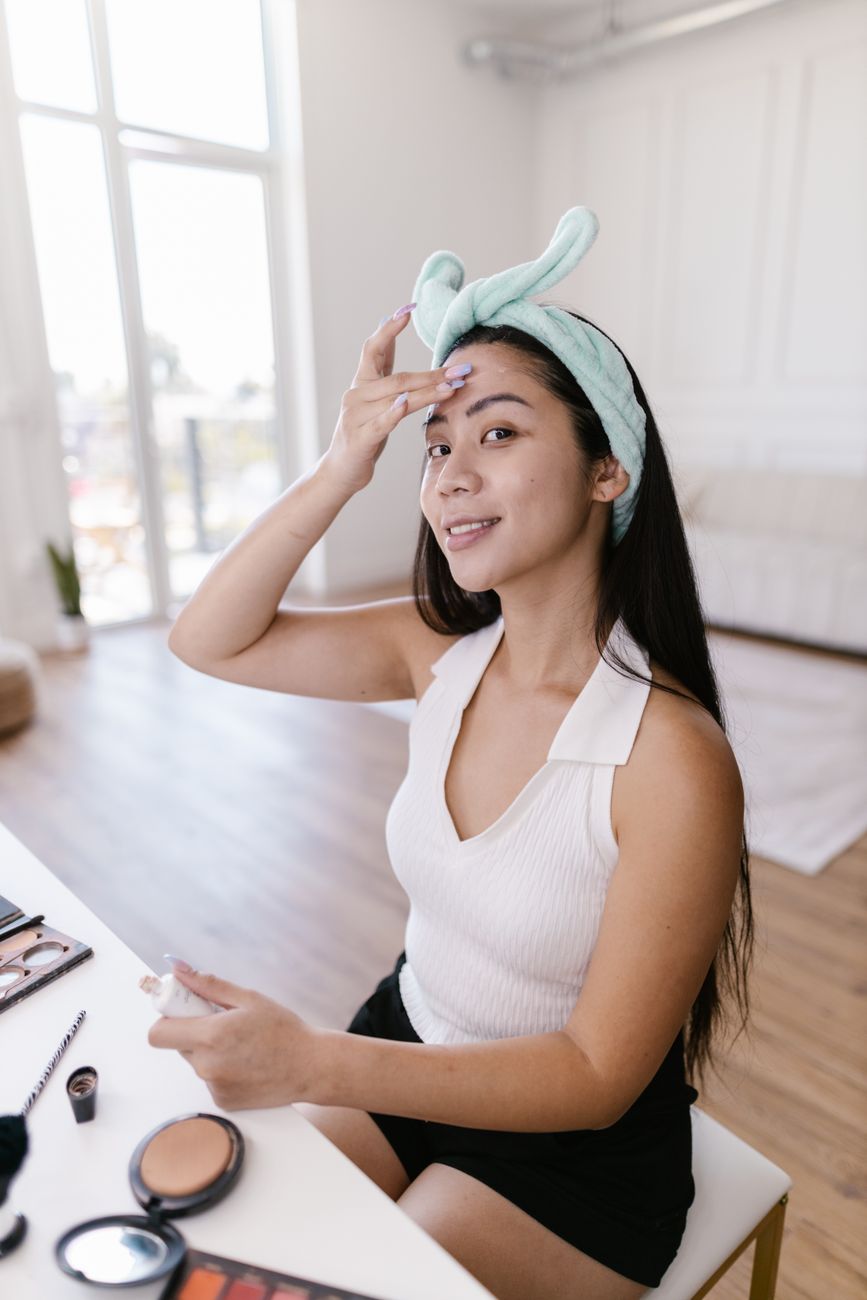 Smiling woman applies skincare product, demonstrating a beauty routine in her cozy home.