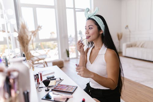 Free Long Haired Brunette Putting on Makeup in a Bright Interior Stock Photo