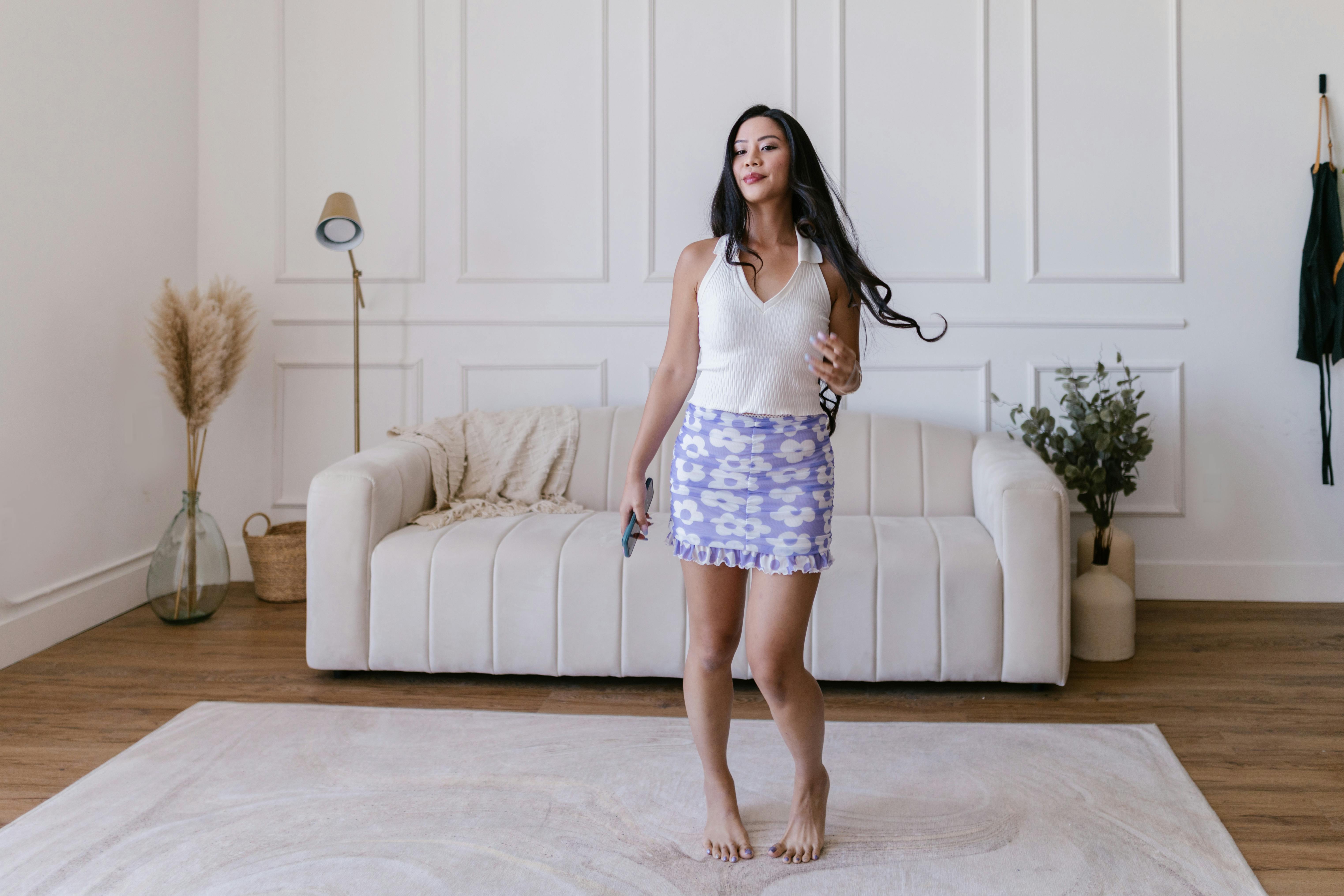 long haired woman in short skirt posing with bare feet on a white carpet