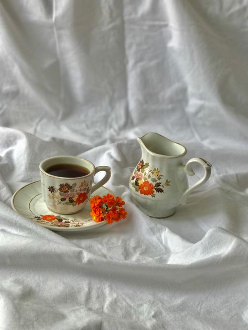 Free A floral-patterned teacup and creamer with orange flowers on white fabric. Stock Photo