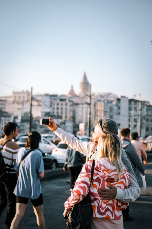 Free Couple taking a selfie in İstanbul with Galata Tower in the background. Urban street vibe, people around. Stock Photo