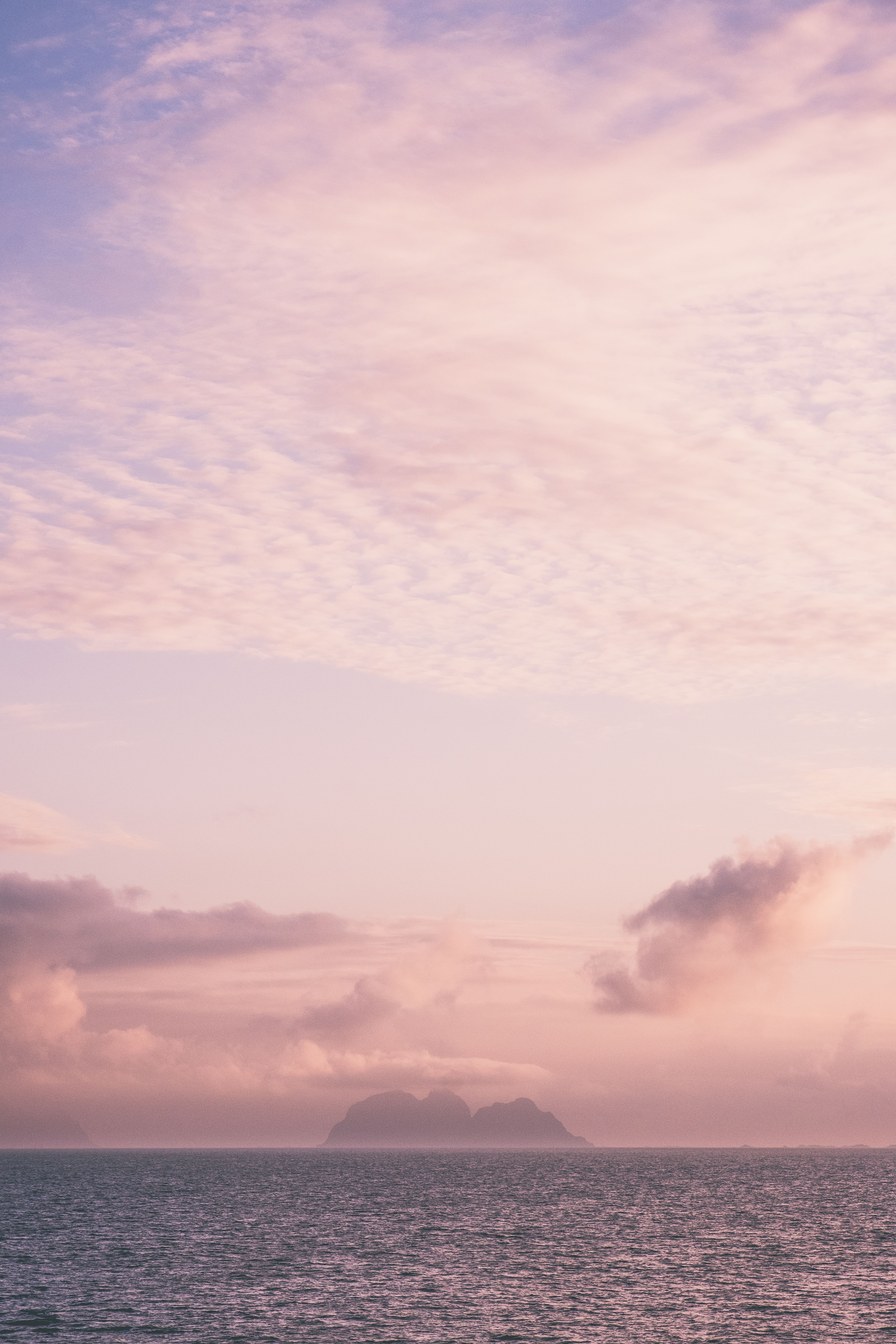A tranquil view of the Norwegian Sea at sunset with pastel skies and distant islands.