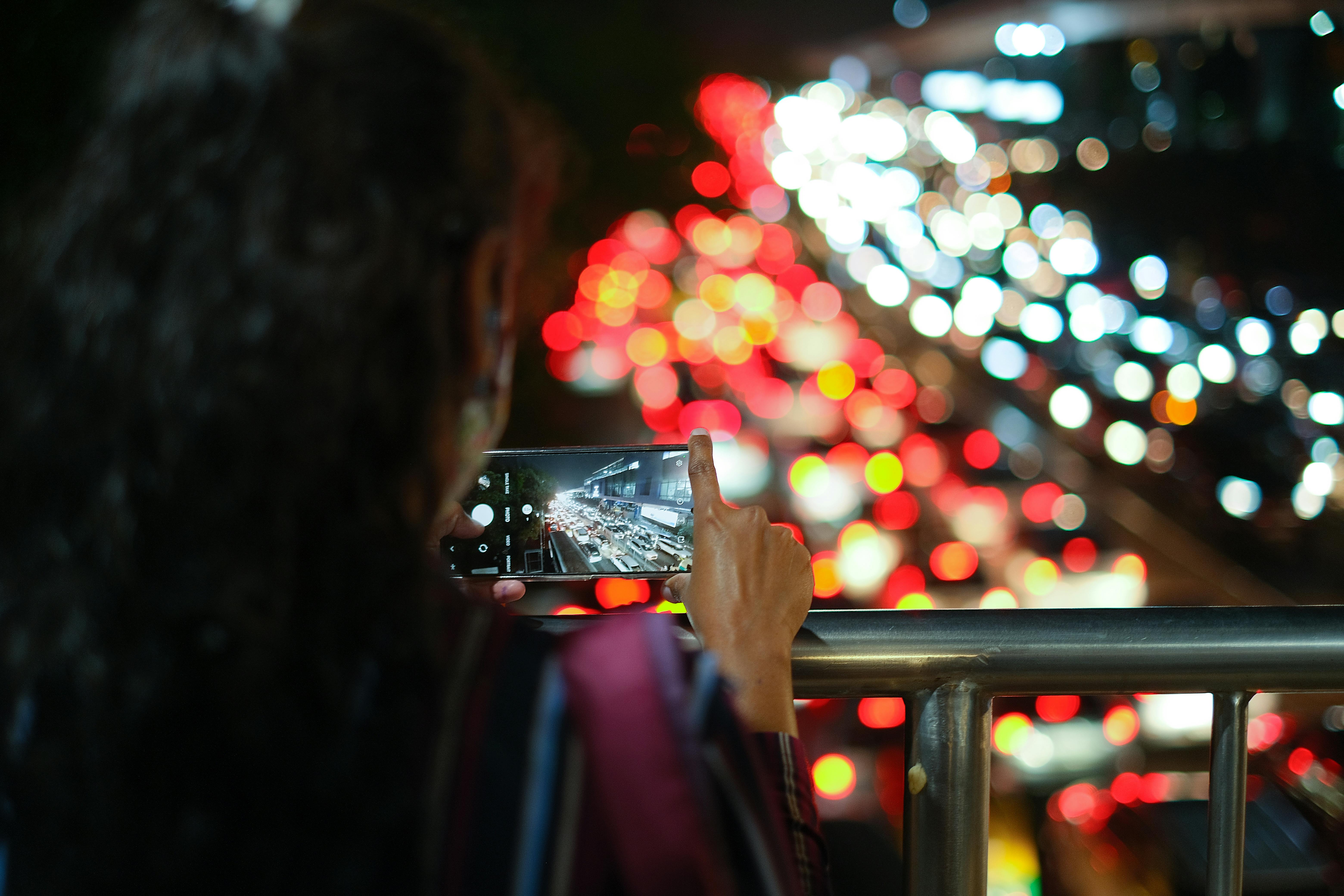 A person photographing vibrant night traffic in New Delhi with a smartphone.
