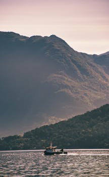A tranquil scene of a single boat on Hardanger Fjord with mountains in the background under a pastel sky.