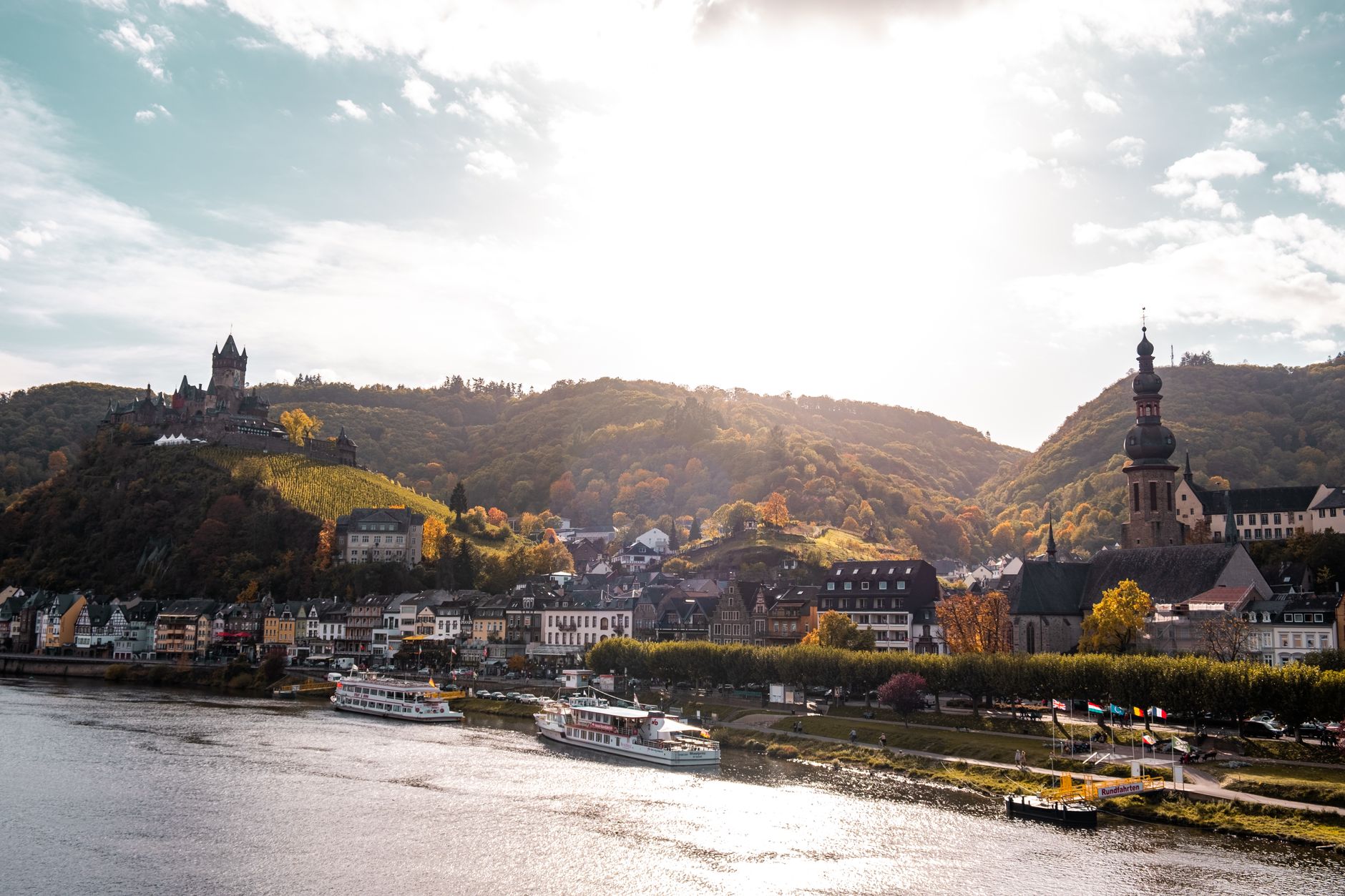 Charmante Herbstlandschaft von Cochem, Deutschland, mit Schloss, Fluss und Hügeln unter einem hellen Himmel.
