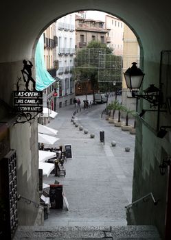 View through Arch of Cuchilleros in Madrid, showcasing a vibrant street scene with cafes.