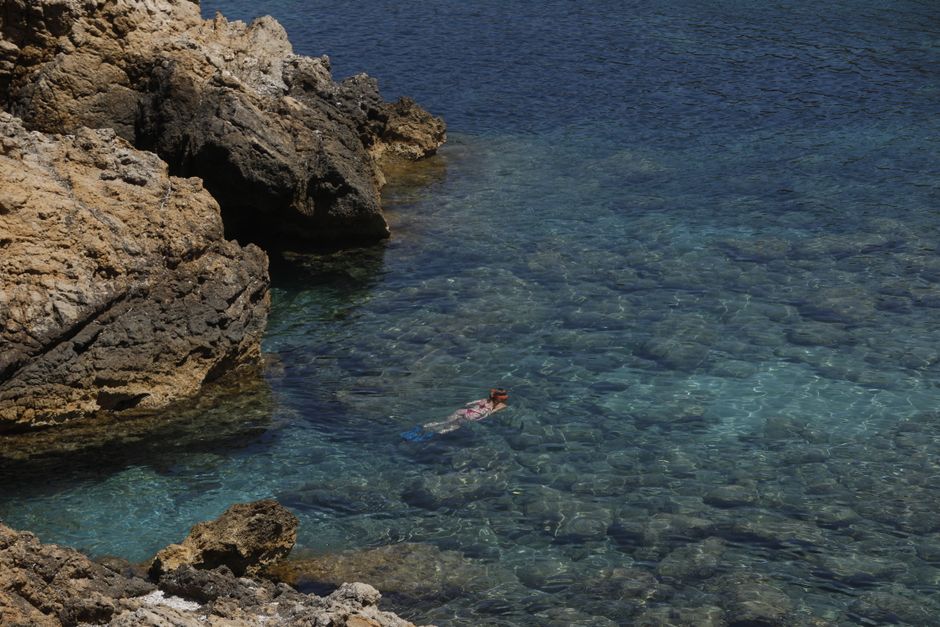 Woman snorkeling near rocky shore in Ibiza's crystal-clear waters, enjoying a summer day.