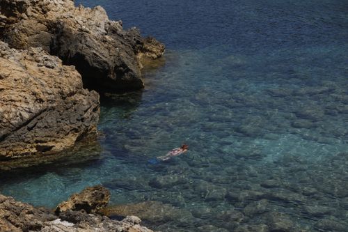 Free Woman snorkeling near rocky shore in Ibiza's crystal-clear waters, enjoying a summer day. Stock Photo