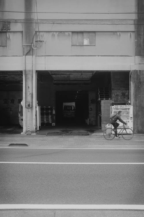 Grayscale Photo of Man Riding Bicycle on Road