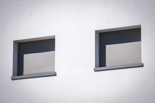 Close-up of a white wall showcasing two sunlit windows with minimalistic design.