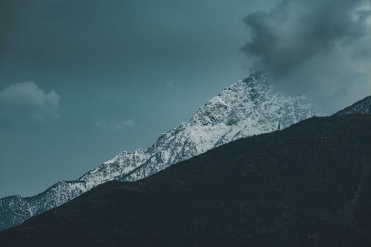 A breathtaking view of a snow-covered mountain peak shrouded in clouds against a moody sky.