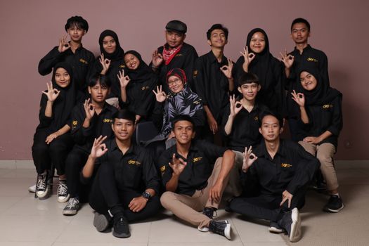 Diverse group of teenagers and a mature woman posing in black outfits, making hand signs.