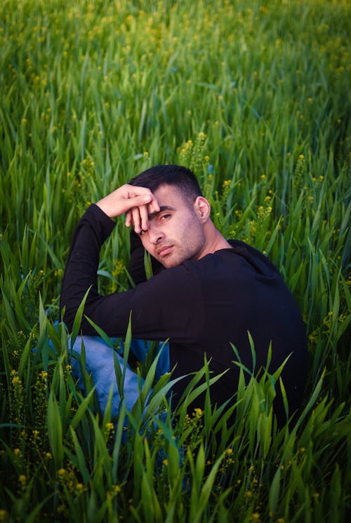 Man in Black Long Sleeve Shirt Sitting on Green Grass Field