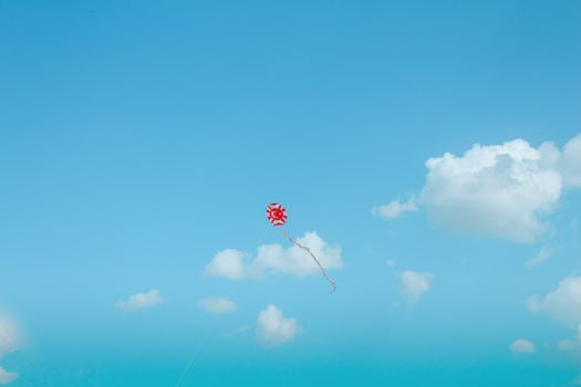 A vibrant red kite soaring in a clear blue sky with fluffy clouds.